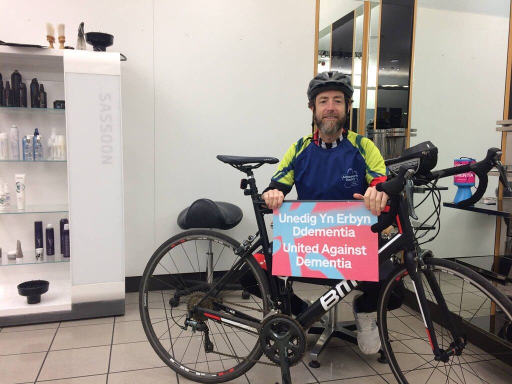 Chris posing with his bike and a "United against Dementia" poster