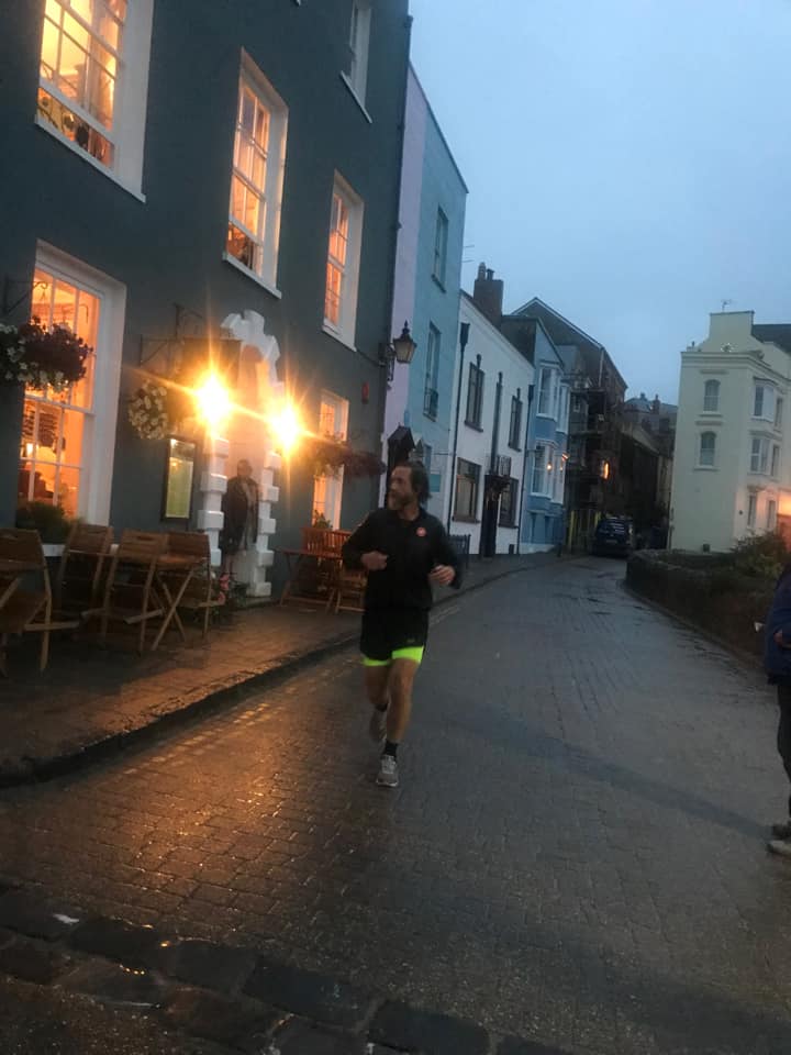 Chris running through Tenby town centre. He's dressed in all black running kit.
